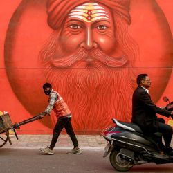 Un trabajador empuja una carretilla que transporta basura, pasando por un mural en la pared antes del festival Maha Kumbh Mela en Prayagraj, India. | Foto:NIHARIKA KULKARNI / AFP