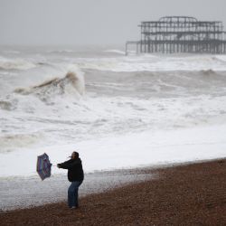 Una mujer sostiene su paraguas roto mientras camina por la playa de Brighton, en el sur de Inglaterra, con el West Pier de fondo, cuando se emitieron advertencias meteorológicas por lluvia, nieve y viento en todo el Reino Unido. | Foto:HENRY NICHOLLS / AFP