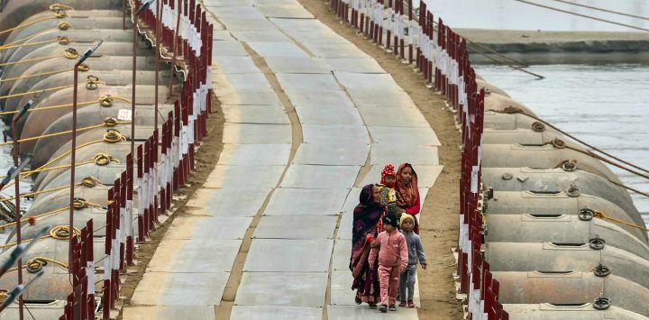 Mujeres y niños caminan sobre un puente flotante sobre el río Ganges, en una fría tarde de invierno, antes del festival Maha Kumbh Mela en Prayagraj, India.