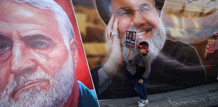 Un niño pasa junto a una fotografía del líder libanés de Hezbolá, Hassan Nasrallah (derecha), y del comandante de la Guardia Revolucionaria iraní, Qasem Soleimani, durante una manifestación en la zona de Shula, al oeste de Bagdad.