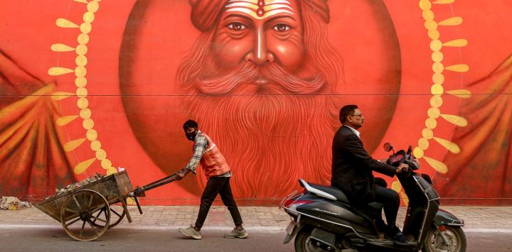 Un trabajador empuja una carretilla que transporta basura, pasando por un mural en la pared antes del festival Maha Kumbh Mela en Prayagraj, India.