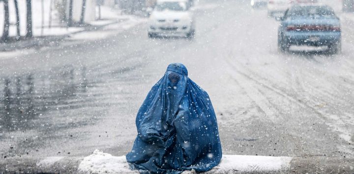 Una mujer afgana vestida con burka busca limosna en una calle durante la primera nevada intensa de este invierno en Kabul.