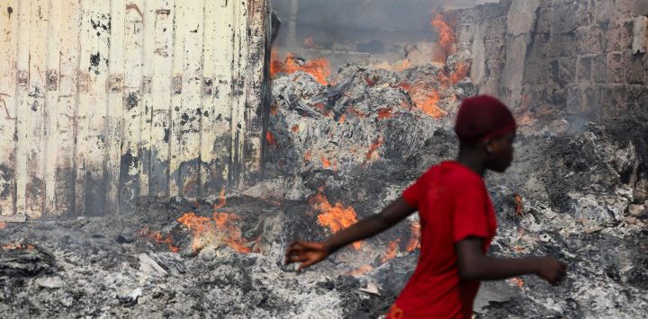 Una mujer pasa junto a un incendio en el mercado de ropa de segunda mano de Kantamanto, en Accra, Ghana.