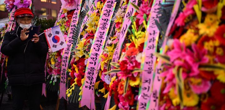 Una persona se encuentra junto a flores y mensajes en apoyo al presidente de Corea del Sur destituido, Yoon Suk Yeol, durante una manifestación cerca de su residencia en Seúl. Miles de manifestantes surcoreanos desafiaron una tormenta de nieve por el presidente suspendido Yoon Suk Yeol, quien todavía se resistía al arresto por un intento fallido de instaurar la ley marcial menos de 48 horas antes de que expirara la orden judicial.