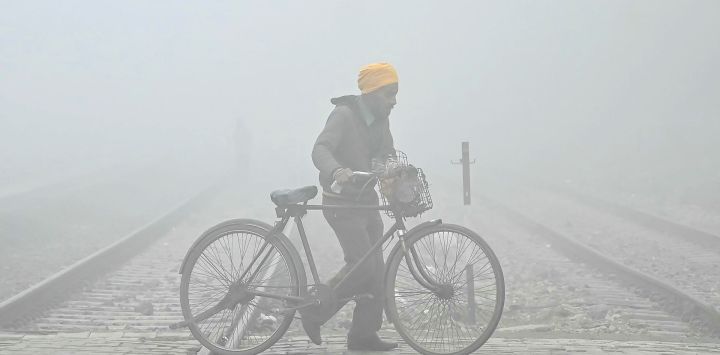 Un ciclista cruza las vías del tren en medio de una densa niebla en una fría mañana de invierno en Amritsar, India.