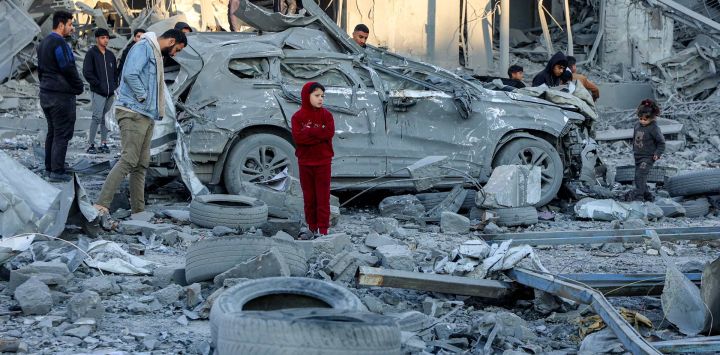 Hombres y niños junto a un automóvil destruido entre escombros y escombros junto a un edificio derrumbado en el lugar del bombardeo israelí en un bloque residencial en la calle Jalaa en la ciudad de Gaza, en medio de la guerra en curso en el territorio palestino entre Israel y Hamás.