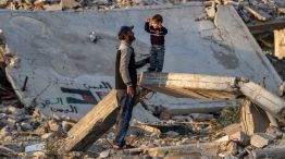 20250117 Un hombre habla con un niño de pie sobre una viga de hormigón rota junto a los escombros de un edificio derrumbado en un campamento para desplazados por el conflicto en Bureij, en el centro de la Franja de Gaza