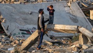 20250117 Un hombre habla con un niño de pie sobre una viga de hormigón rota junto a los escombros de un edificio derrumbado en un campamento para desplazados por el conflicto en Bureij, en el centro de la Franja de Gaza