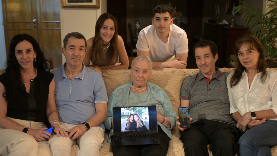 Holocaust survivor Raquel Lily Soriano Alhadeff (C), 97, poses surrounded by part of her family (some living in the US and UK): her son Anthony (2nd L) and his wife Betina (L), her son James (2nd R) and his wife Silvana (R), her grandchildren Cindy (3rd L) and Tomas (3rd R), and (on laptop and mobile screens) her granddaughters Chiara, Nicole, and Barbara, during an interview with AFP in Buenos Aires on December 23, 2024.