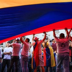 Ciudadanos venezolanos ondean una bandera venezolana gigante mientras participan en una manifestación a favor del líder opositor Edmundo González Urrutia en Lima. | Foto:CONNIE FRANCE CALDERON MARTEL / AFP