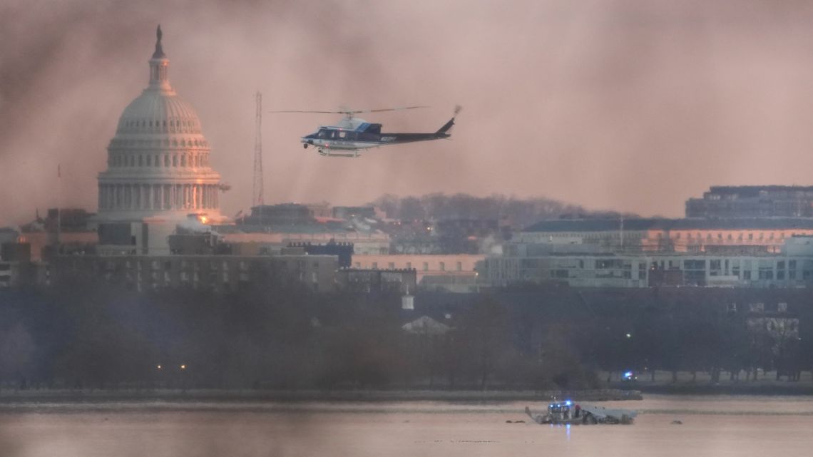 A helicopter flies near the crash site of the American Airlines plane on the Potomac River after the plane crashed on approach to Reagan National Airport on January 30, 2025 in Arlington, Virginia.