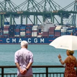 La gente camina mientras se ve un barco de carga atracado en la terminal del puerto de Pasir Panjang en Singapur. | Foto:Roslan Rahman / AFP