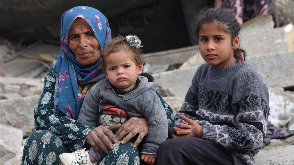 A Palestinian woman and children sit amid the rubble of destroyed buildings at Saftawi street in Jabalia, in the northern Gaza Strip, on February 5, 2025 during a ceasefire deal in the war between Israel and Hamas.