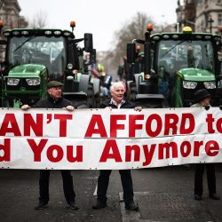 Los agricultores sostienen una pancarta que dice "Ya no podemos permitirnos alimentarlos" mientras se encuentran frente a tractores estacionados en Whitehall durante una manifestación de agricultores para protestar contra los cambios en las reglas del impuesto a la herencia para la propiedad de la tierra para los agricultores, en el centro de Londres. | Foto:HENRY NICHOLLS / AFP