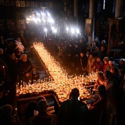 Los creyentes encienden velas en una plataforma en forma de cruz cubierta con velas unidas a frascos de miel durante una ceremonia que conmemora el día de San Haralampi, santo patrón ortodoxo de los apicultores, en la Iglesia de la Santísima Virgen en Blagoevgrad, este de Bulgaria. | Foto:NIKOLAY DOYCHINOV / AFP