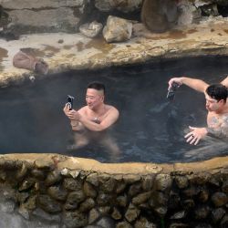 Esta fotografía muestra a tres hombres tomando un baño termal al aire libre burlándose de un macaco japonés, comúnmente llamado "mono de nieve", en el parque de monos Jigokudani (Valle del Infierno) en la ciudad de Yamanouchi, prefectura de Nagano. | Foto:Mladen Antonov / AFP