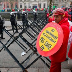 Un manifestante con un cartel redondo que dice "los funcionarios no cederán" junto a la policía antidisturbios mientras los trabajadores participan en una protesta nacional convocada por los sindicatos contra el plan del nuevo gobierno de reformar los regímenes especiales de pensiones, en Bruselas. | Foto:NICOLAS TUCAT / AFP