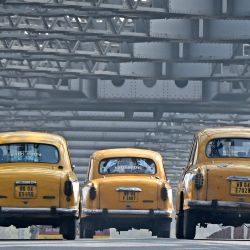 Esta fotografía muestra a pasajeros que viajan en taxis amarillos Hindustan Ambassador a lo largo del puente Howrah en Calcuta, India. | Foto:DIBYANGSHU SARKAR / AFP