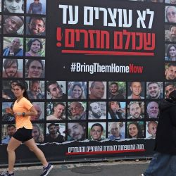 La gente pasa frente a un cartel con los retratos de los rehenes israelíes retenidos en la Franja de Gaza desde los ataques del 7 de octubre de 2023 por militantes de Hamás, en Jerusalén, cuando el país conmemora el 500º día desde su secuestro. | Foto:AHMAD GHARABLI / AFP