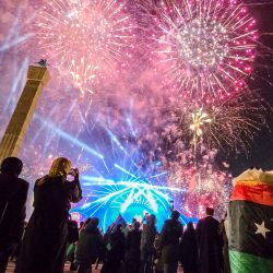 La gente observa un espectáculo de fuegos artificiales durante las conmemoraciones del 14º aniversario del levantamiento que derrocó al líder libio Muammar Kadhafi en la Plaza de los Mártires de la capital libia, Trípoli. | Foto:AFP
