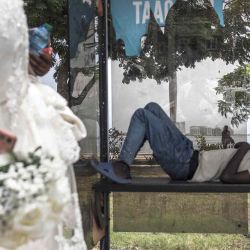 Un hombre duerme en un banco mientras pasa una novia, que vino a tomarse fotografías junto a los invitados a la boda en el paseo marítimo, en Luanda. Foto de MARCO LONGARI / AFP | Foto:AFP