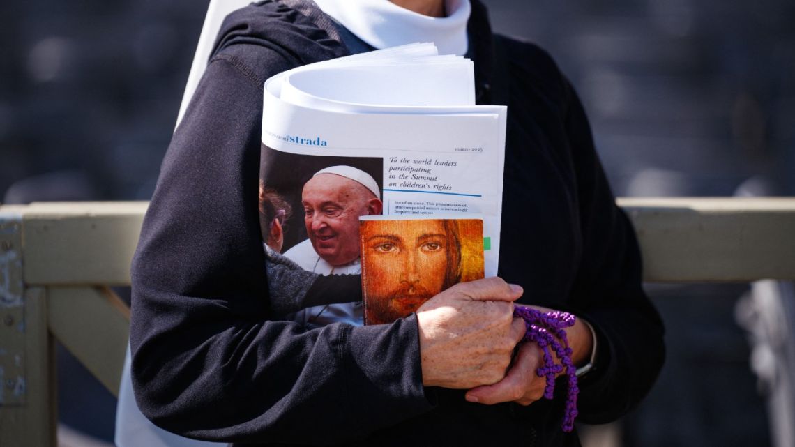 A nun walks with the 'L'Osservatore Romano' newspaper under her arm, featuring an image of Pope Francis, who remains hospitalised.