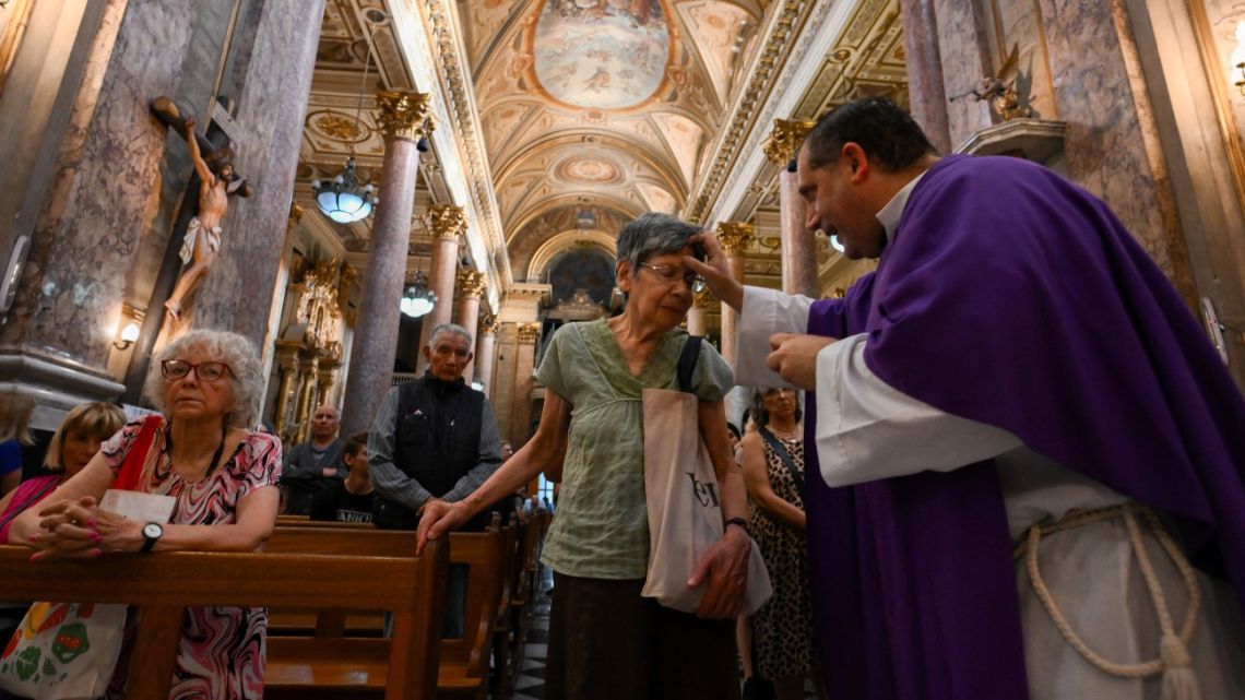 A priest makes the sign of the cross on the forehead of a faithful during the celebration of Ash Wednesday at the Basilica San Josép de Flores in Buenos Aires on March 5, 2025. The Basilica de San Jose de Flores was the church where Pope Francis was inspired to consecrate his life to God and the Catholic Church. Pope Francis's condition was stable on Wednesday as he neared three weeks in the hospital battling pneumonia, a Vatican source said, with celebrations for the Lent religious season starting without him. 