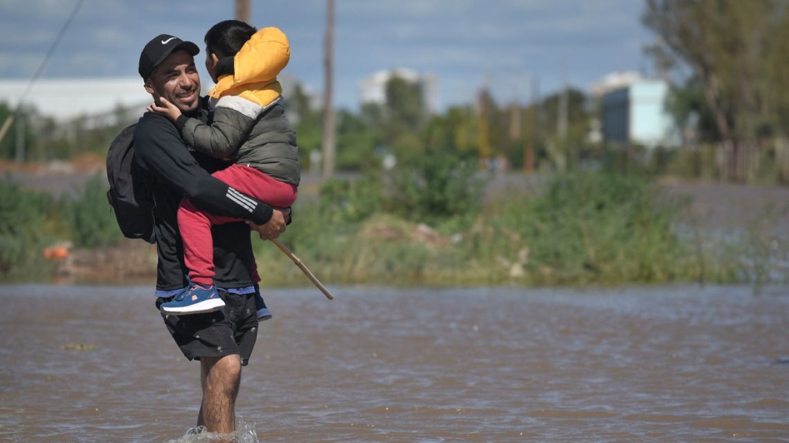 A man carrying a child walks through flooded waters the day after a heavy storm in Bahía Blanca, 600 kilometres south of Buenos Aires on March 8, 2025.