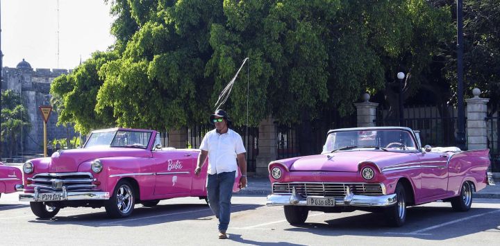 Imagen de un hombre caminando entre dos automóviles antiguos estacionados en una calle, en La Habana, capital de Cuba.