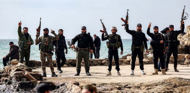 Miembros de las fuerzas de seguridad leales al gobierno interino sirio posan con sus armas de fuego en la costa del mar Mediterráneo en la ciudad occidental de Latakia, en Siria.