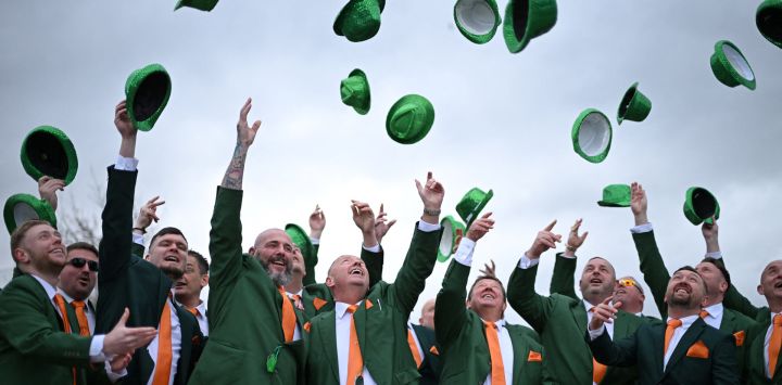 Los aficionados a las carreras, vestidos con los colores irlandeses, lanzan sus sombreros al aire mientras se celebra el Día de San Patricio en el hipódromo de Cheltenham, en Cheltenham, oeste de Inglaterra.