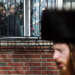 Niños miran por la ventana mientras la gente camina por la calle durante la celebración de Purim en el barrio de Williamsburg, en el distrito de Brooklyn, Nueva York. | Foto:CHARLY TRIBALLEAU / AFP
