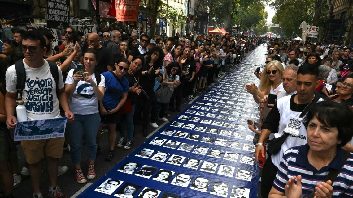 People stand next to a large banner with portraits of people who disappeared during Argentina's 1976-1983 military dictatorship while heading to Plaza de Mayo Square to commemorate the 49th anniversary of the military coup in Buenos Aires on March 24, 2025. 