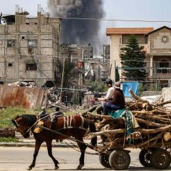 Hombres en una carreta tirada por caballos, observan cómo una columna de humo se eleva desde un edificio alcanzado por un bombardeo israelí. Foto de Eyad BABA / AFP | Foto:AFP