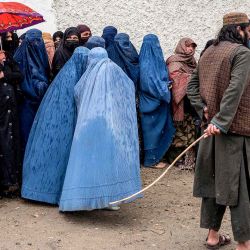 Guardia mientras mujeres afganas con burka hacen fila bajo un diluvio para recibir alimentos donados durante el mes sagrado islámico de Ramadán. Foto de Wakil KOHSAR / AFP | Foto:AFP