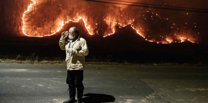 Un hombre habla con su hijo por teléfono bajo una farola en la calle frente a su casa mientras los incendios forestales arden en Uiseong, Corea del Sur. Foto de YASUYOSHI CHIBA / AFP