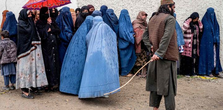 Guardia mientras mujeres afganas con burka hacen fila bajo un diluvio para recibir alimentos donados durante el mes sagrado islámico de Ramadán. Foto de Wakil KOHSAR / AFP