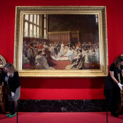 El personal del museo limpia las sillas del trono de Carlhian y Baumetz con la pintura "El matrimonio de Jorge, duque de York, con la princesa María de Teck" del pintor danés Laurits Regner Tuxen durante una vista previa para la prensa de la exposición "Los eduardianos: la era de la elegancia", en la Galería del Rey del Palacio de Buckingham, en el centro de Londres. | Foto:HENRY NICHOLLS / AFP