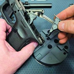 Despiece interno de una pistola, donde se aprecian el armazón, el cañón y la cola del disparador con su resorte y mecanismo, entre  otros componentes.