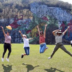 Imagen de jóvenes turistas saltando frente al Mural de la Prehistoria, una obra de 80 metros de altura por 120 de ancho hecha sobre las rocas para representar el pasado geológico y biológico de la región, en el valle de Viñales, en la provincia de Pinar del Río, Cuba. | Foto:Xinhua/Joaquín Hernández
