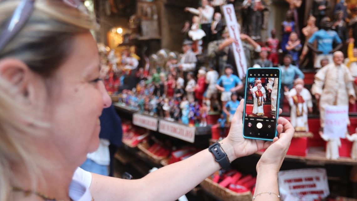 A pedestrian uses a smartphone to take a picture of a statue of newly elected Pope Leo XIV displayed at the shop of Gennaro Di Virgilio in San Gregorio Armeno Alley, a street where craftsmen of traditional Napolitan Christmas Crib figurines have workshops, in Naples, on May 9, 2025. 