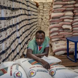 Un trabajador descansa sobre sacos de ayuda apilados en una tienda de campaña mientras refugiados congoleños esperan la oportunidad de recibir asistencia durante una operación de distribución de alimentos en el campamento de refugiados de Musenyi, en Giharo. | Foto:LUIS TATO / AFP