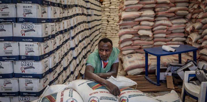 Un trabajador descansa sobre sacos de ayuda apilados en una tienda de campaña mientras refugiados congoleños esperan la oportunidad de recibir asistencia durante una operación de distribución de alimentos en el campamento de refugiados de Musenyi, en Giharo.
