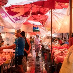 Una mujer con impermeable observa un puesto de carne fresca en el mercado de Khlong Toei durante una tormenta en Bangkok, Tailandia. | Foto:Chanakarn Laosarakham / AFP
