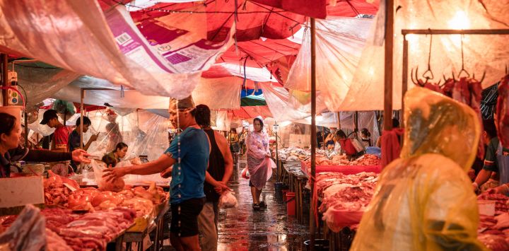 Una mujer con impermeable observa un puesto de carne fresca en el mercado de Khlong Toei durante una tormenta en Bangkok, Tailandia.