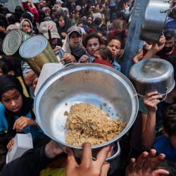 Palestinos se reúnen para recibir una comida caliente en un punto de distribución de alimentos en el campamento de refugiados de Nuseirat, en el centro de la Franja de Gaza. Los gazatíes esperaban desesperadamente suministros vitales después de que Israel declarara haber permitido la entrada de decenas de camiones de la ONU, pero se enfrentaba a una creciente presión internacional para aumentar el flujo de ayuda y abandonar su intensificada campaña militar. | Foto:Eyad Baba / AFP