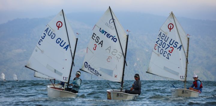 Imagen de las veleristas Nataly Dutoit, de Guatemala, Ariana Zuriel, de El Salvador, y Amelia Graham, de Estados Unidos, compitiendo en la categoría Optimist Femenino, durante la segunda edición del "FesaVela International Regatta 2025" en el Lago de Ilopango, en el departamento de San Salvador, capital de El Salvador.