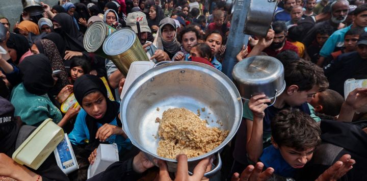 Palestinos se reúnen para recibir una comida caliente en un punto de distribución de alimentos en el campamento de refugiados de Nuseirat, en el centro de la Franja de Gaza. Los gazatíes esperaban desesperadamente suministros vitales después de que Israel declarara haber permitido la entrada de decenas de camiones de la ONU, pero se enfrentaba a una creciente presión internacional para aumentar el flujo de ayuda y abandonar su intensificada campaña militar.