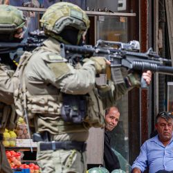 Soldados del ejército israelí apuntan con sus rifles mientras palestinos sentados frente a una tienda observan durante una redada en Nablus, Cisjordania ocupada. | Foto:JAAFAR ASHTIYEH / AFP