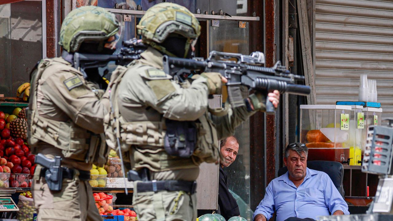 Soldados del ejército israelí apuntan con sus rifles mientras palestinos sentados frente a una tienda observan durante una redada en Nablus, Cisjordania ocupada. | Foto:JAAFAR ASHTIYEH / AFP
